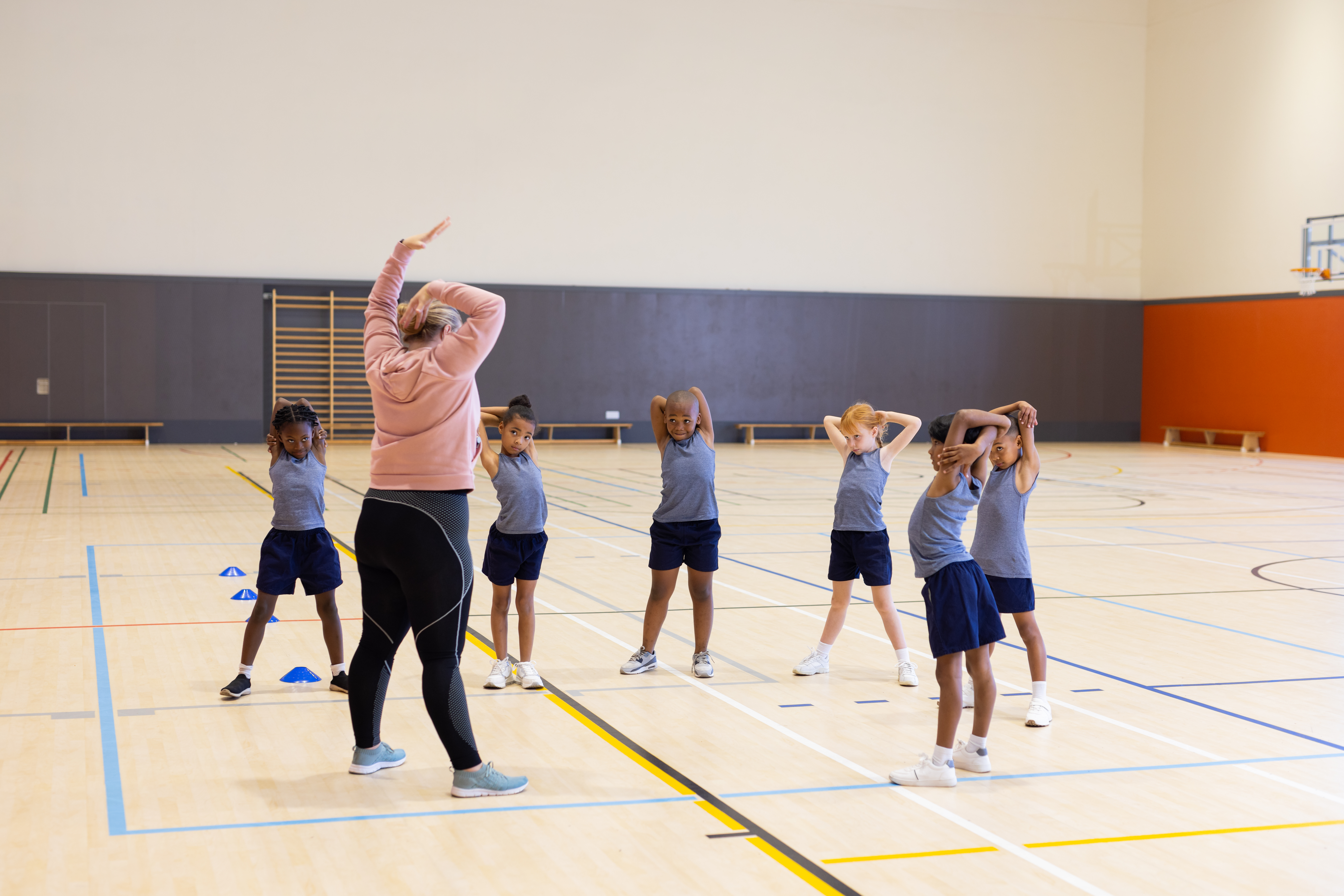 In school gym, diverse children stretching with female teacher during physical education class
