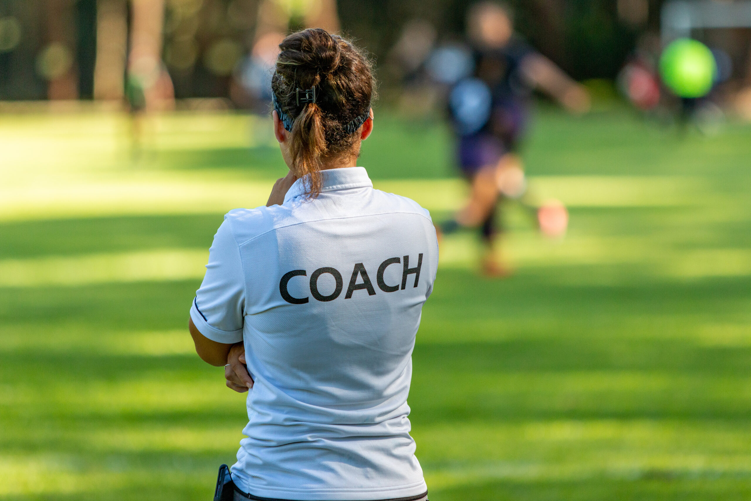 Back view of a female sport coach watching her team compete at a